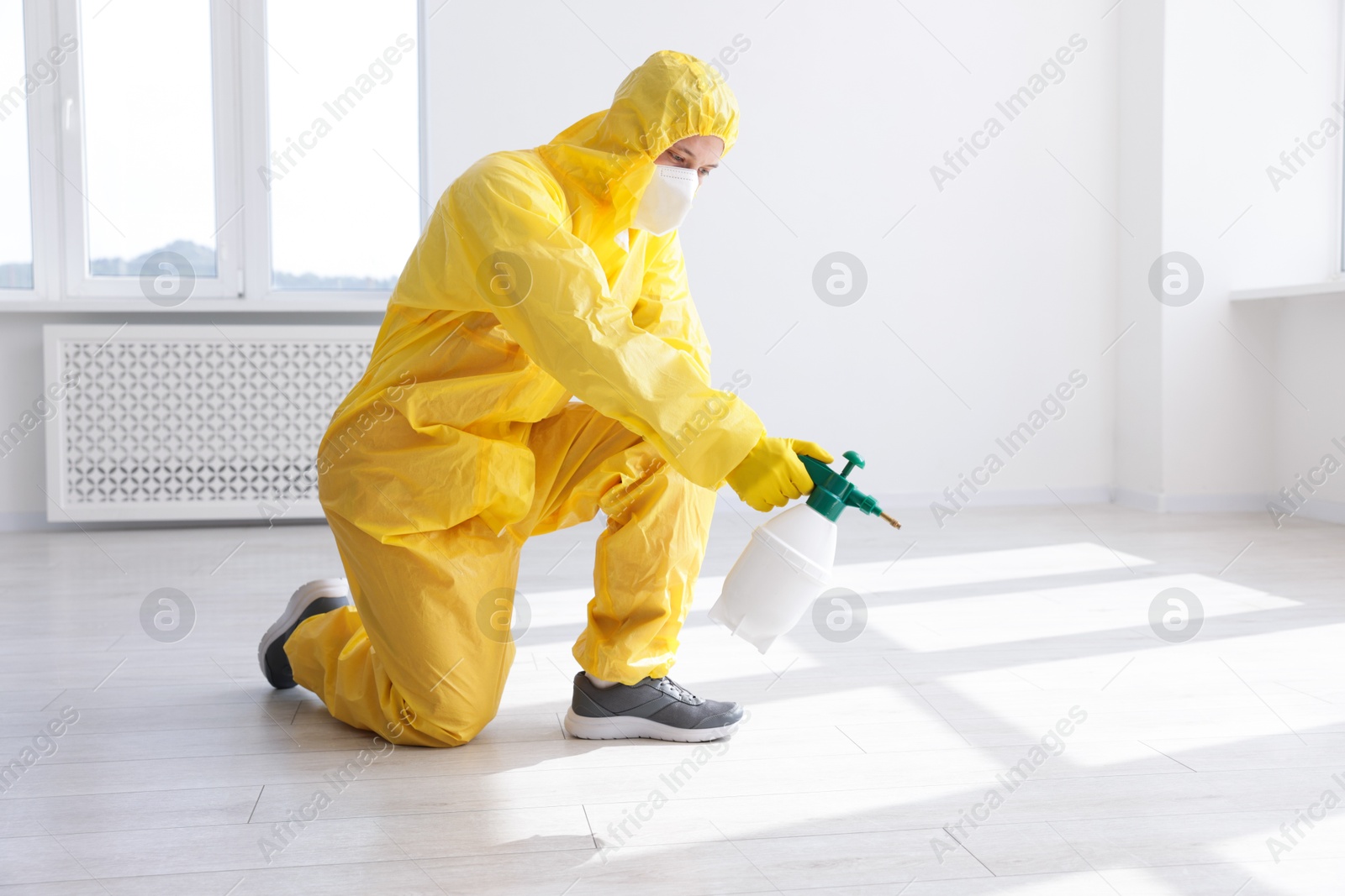 Photo of Pest control worker in protective suit spraying insecticide indoors