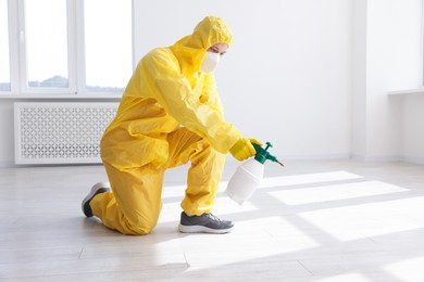 Photo of Pest control worker in protective suit spraying insecticide indoors