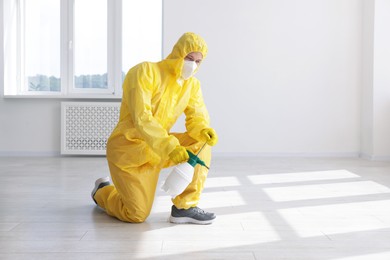 Photo of Pest control worker in protective suit spraying insecticide indoors. Space for text