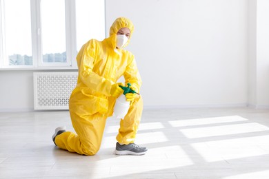 Photo of Pest control worker in protective suit spraying insecticide indoors. Space for text