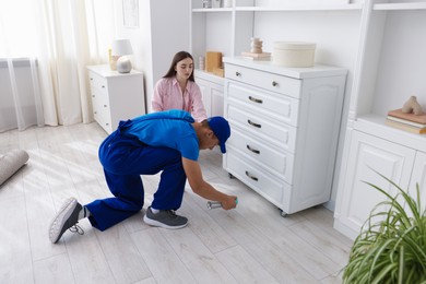 Photo of Worried woman and pest control worker spraying insecticide at home