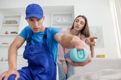 Photo of Worried woman and pest control worker spraying insecticide at home