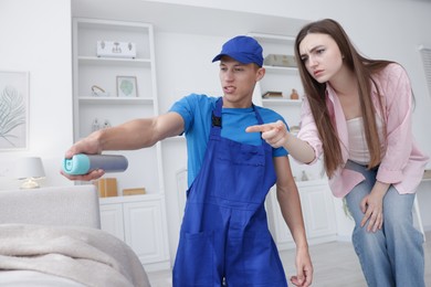 Photo of Worried woman and pest control worker spraying insecticide at home