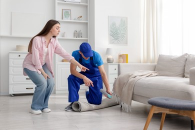 Photo of Worried woman and pest control worker spraying insecticide at home