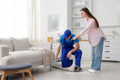 Photo of Worried woman and pest control worker spraying insecticide at home