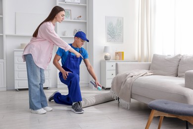 Photo of Worried woman and pest control worker spraying insecticide at home