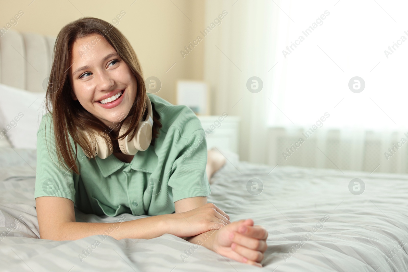 Smiling teenage girl with headphones on bed at home. Space for text Photo of Smiling teenage girl with headphones on bed at home. Space for text