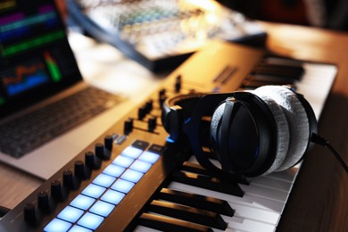 Photo of MIDI keyboard with headphones, laptop and dj mixer on table indoors, closeup