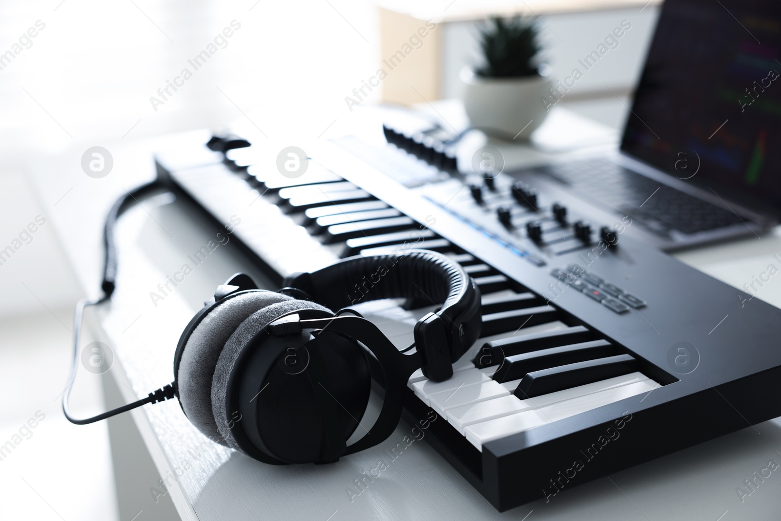 Photo of MIDI keyboard, headphones and laptop on white wooden table indoors, closeup