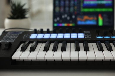 Photo of MIDI keyboard and laptop on table indoors, closeup
