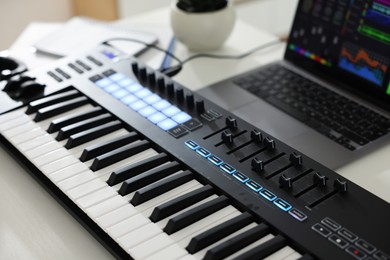 Photo of MIDI keyboard and laptop on white wooden table, closeup