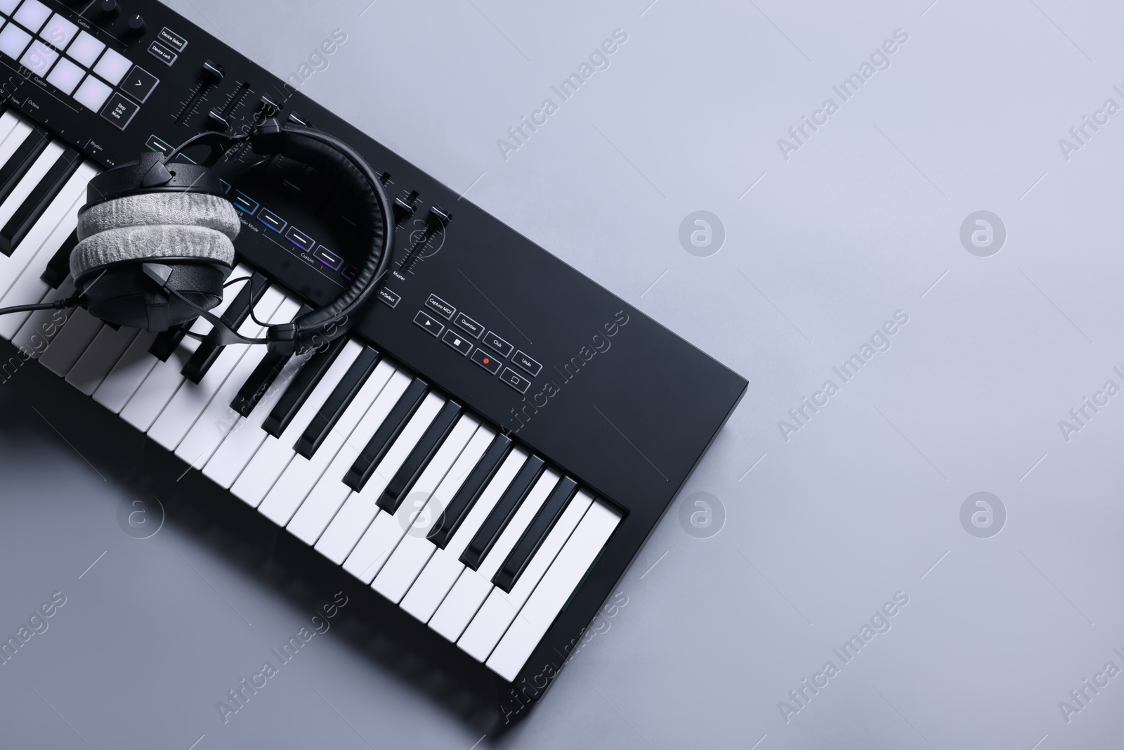MIDI keyboard with headphones on grey background, top view. Space for text Photo of MIDI keyboard with headphones on grey background, top view. Space for text