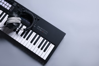 Photo of MIDI keyboard with headphones on grey background, top view. Space for text