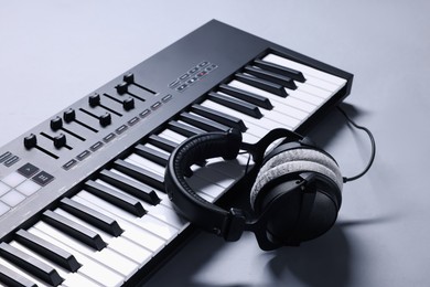 Photo of MIDI keyboard with headphones on grey background, closeup