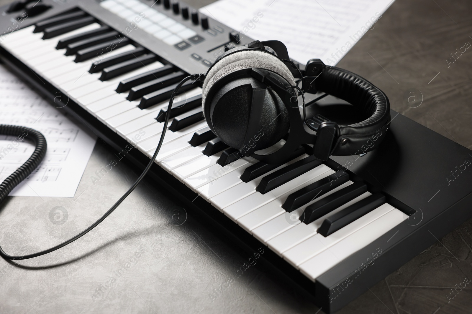 Photo of MIDI keyboard, headphones and music sheets on grey table, closeup