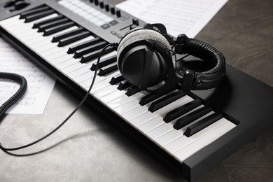 Photo of MIDI keyboard, headphones and music sheets on grey table, closeup