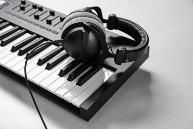 Photo of MIDI keyboard with headphones on white table, closeup. Space for text