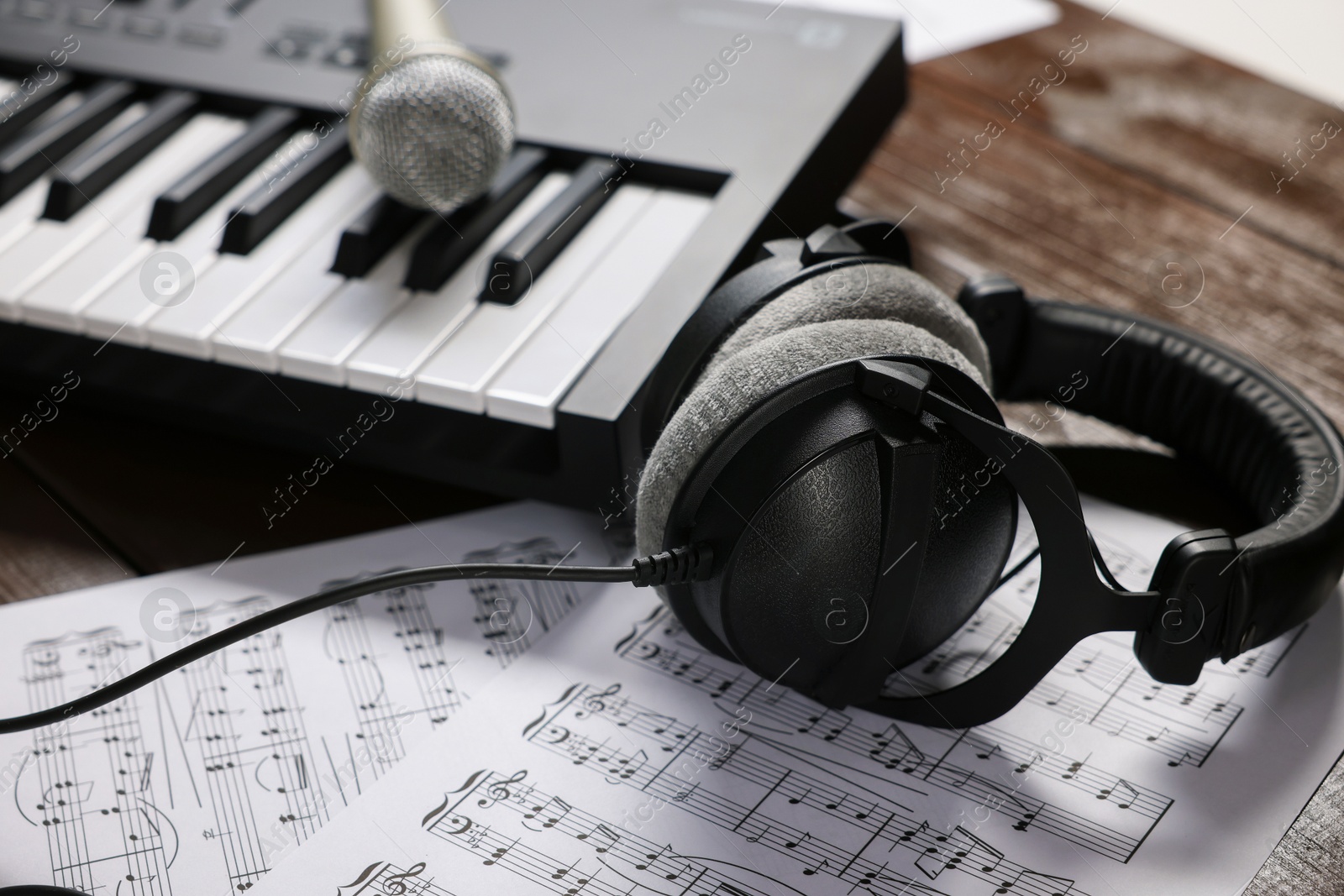 MIDI keyboard, headphones, microphone and music sheets on wooden table, closeup Photo of MIDI keyboard, headphones, microphone and music sheets on wooden table, closeup