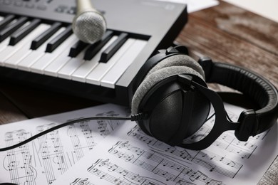 Photo of MIDI keyboard, headphones, microphone and music sheets on wooden table, closeup