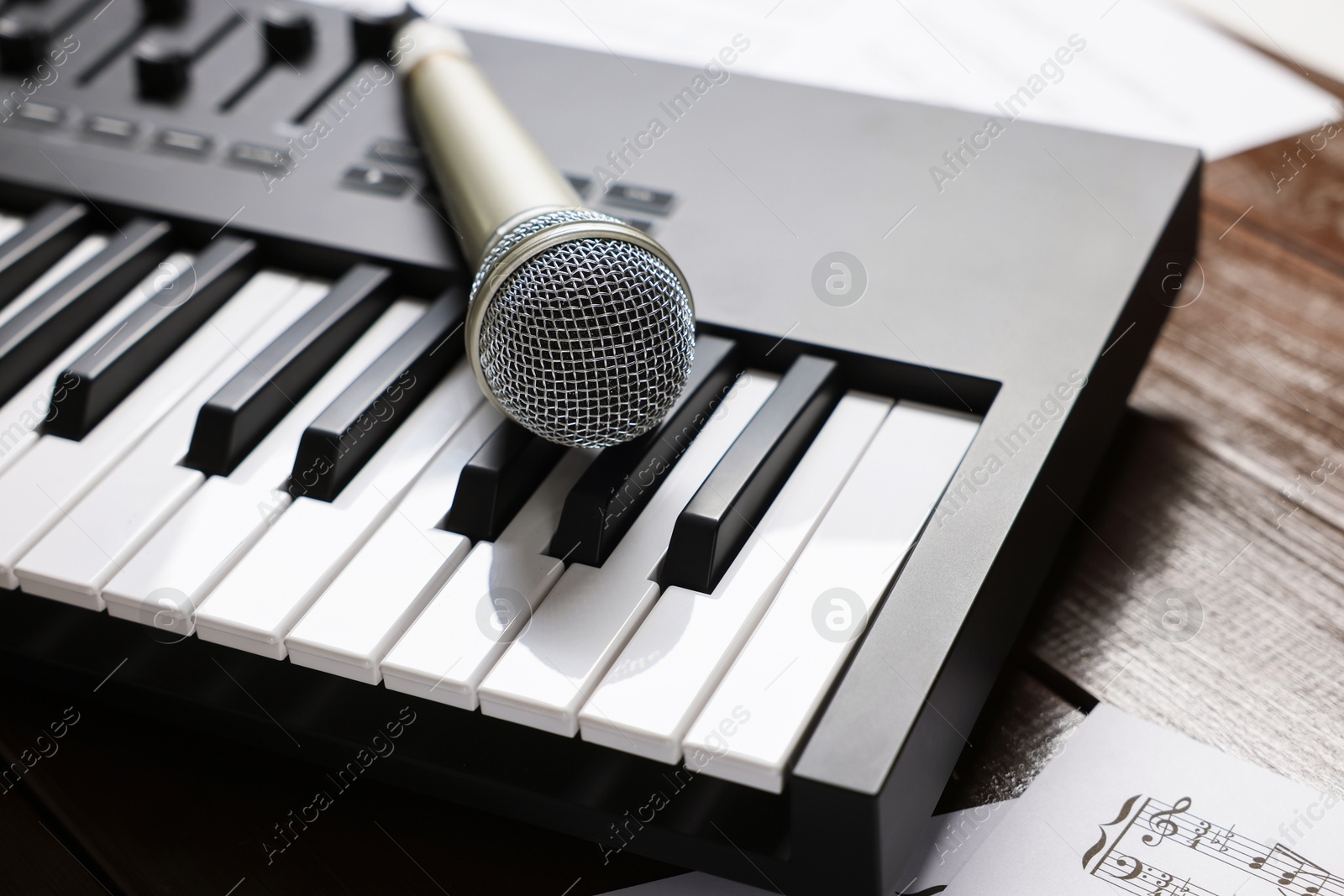 MIDI keyboard, microphone and music sheets on wooden table, closeup Photo of MIDI keyboard, microphone and music sheets on wooden table, closeup