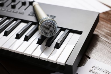 Photo of MIDI keyboard, microphone and music sheets on wooden table, closeup