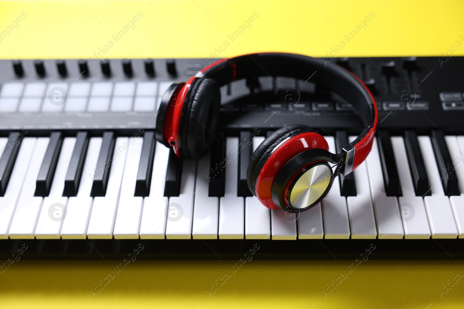 MIDI keyboard with headphones on yellow background, above view Photo of MIDI keyboard with headphones on yellow background, above view