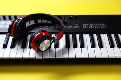 Photo of MIDI keyboard with headphones on yellow background, closeup