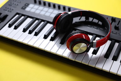 Photo of MIDI keyboard with headphones on yellow background, closeup