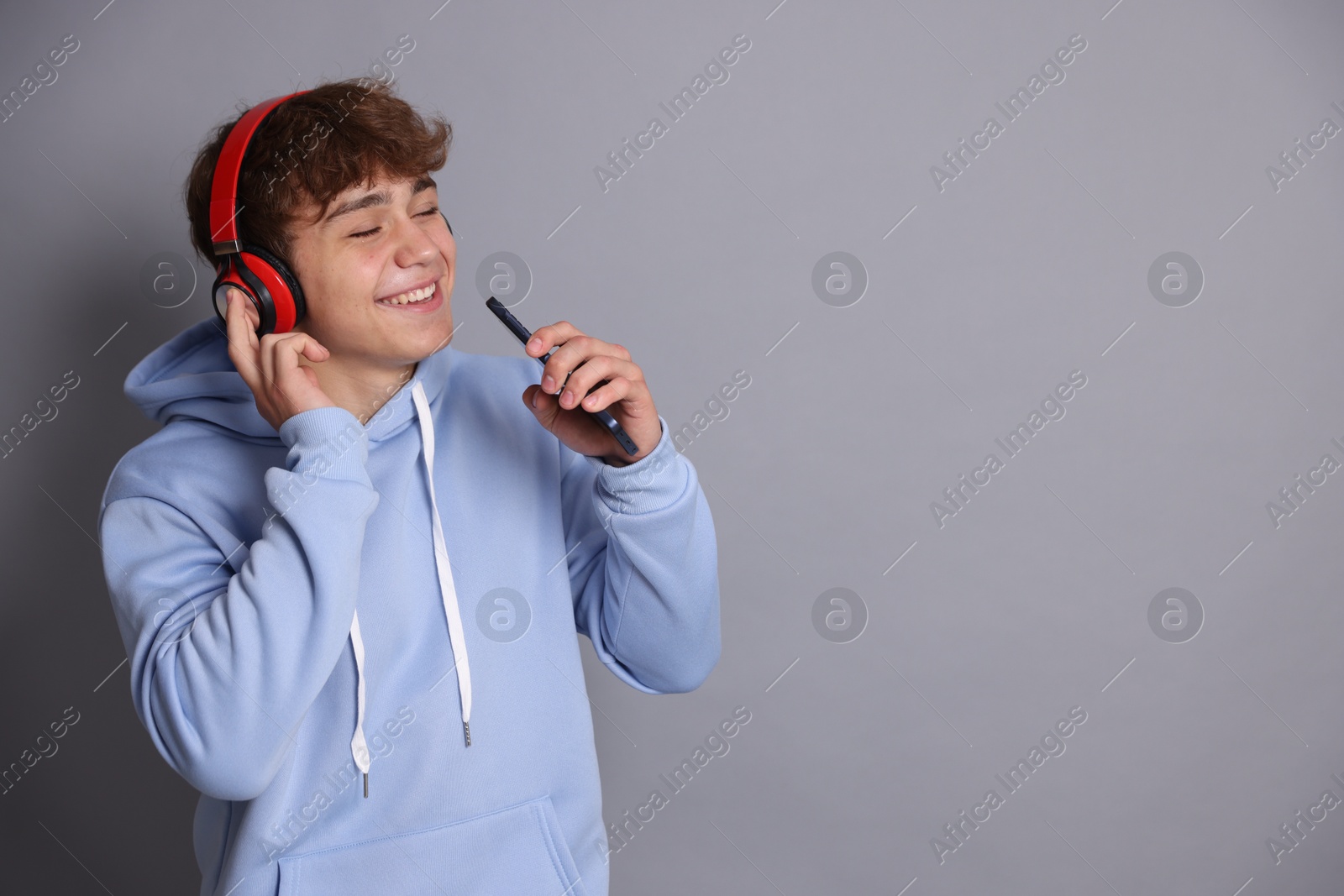 Happy teenage boy in headphones with smartphone singing on grey background. Space for text Photo of Happy teenage boy in headphones with smartphone singing on grey background. Space for text