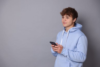 Photo of Teenage boy with smartphone on grey background. Space for text