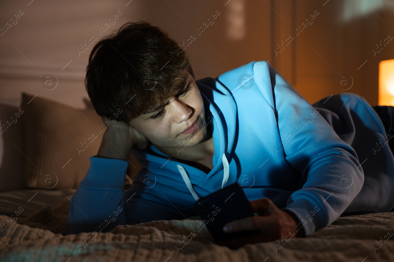 Photo of Teenage boy using smartphone on bed at home