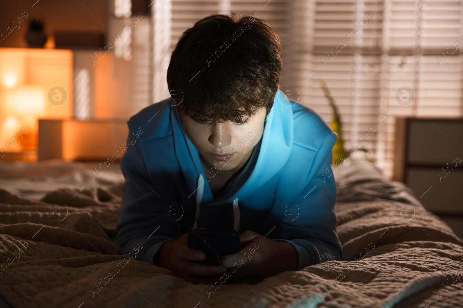 Teenage boy using smartphone on bed at home Photo of Teenage boy using smartphone on bed at home