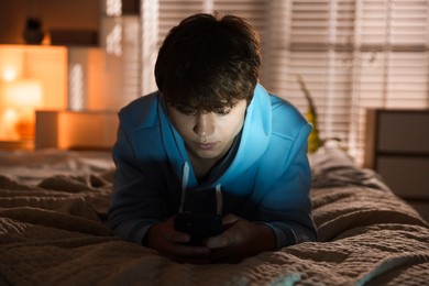 Photo of Teenage boy using smartphone on bed at home