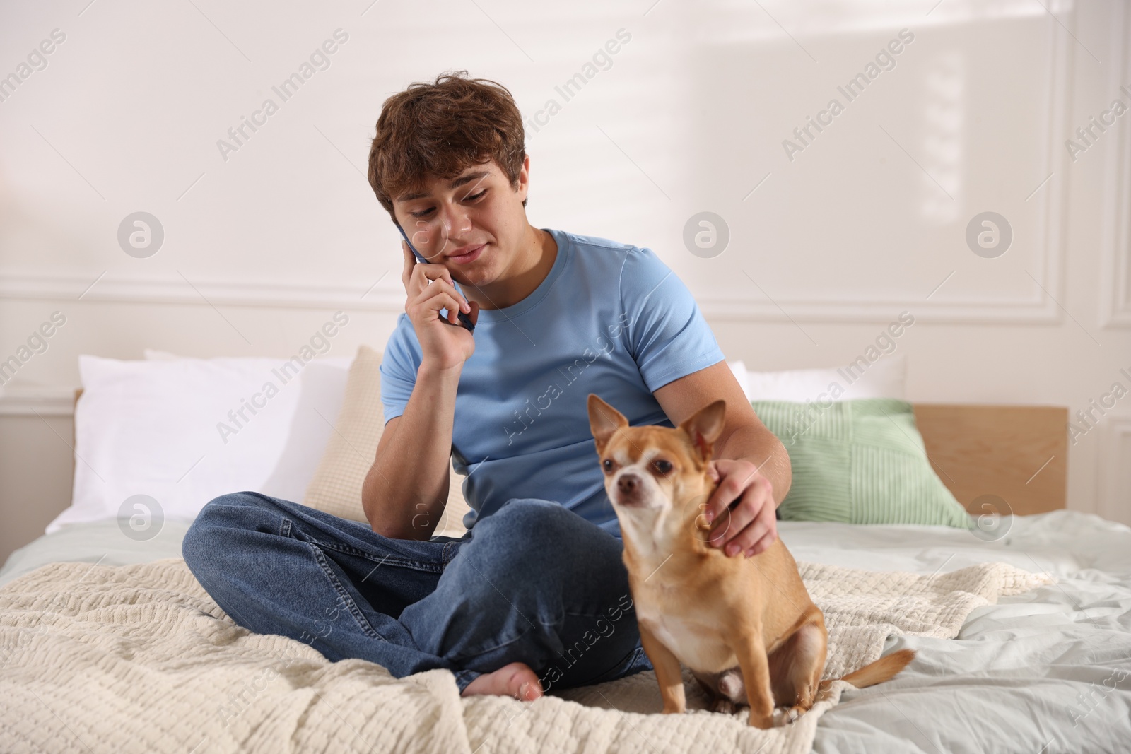 Teenage boy talking by smartphone and dog on bed at home Photo of Teenage boy talking by smartphone and dog on bed at home