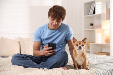 Photo of Teenage boy using smartphone and dog on bed at home