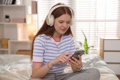 Photo of Teenage girl in headphones using smartphone on bed at home