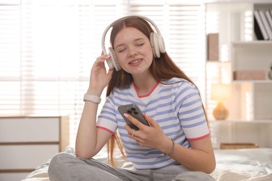 Photo of Smiling teenage girl in headphones with smartphone on bed at home