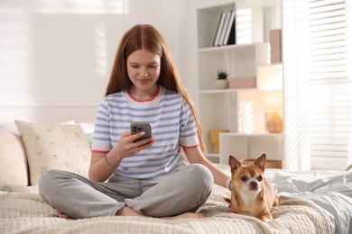 Photo of Teenage girl using smartphone and dog on bed at home