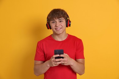 Photo of Smiling teenage boy in headphones with smartphone on yellow background
