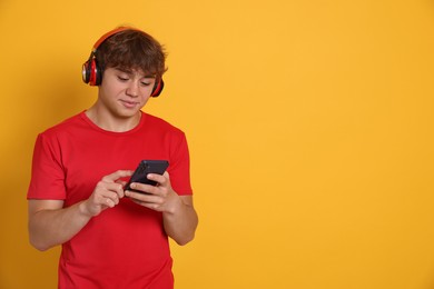 Photo of Teenage boy in headphones using smartphone on yellow background. Space for text