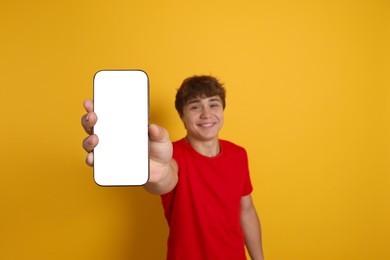Photo of Smiling teenage boy showing smartphone with blank screen on yellow background, selective focus. Mockup for design