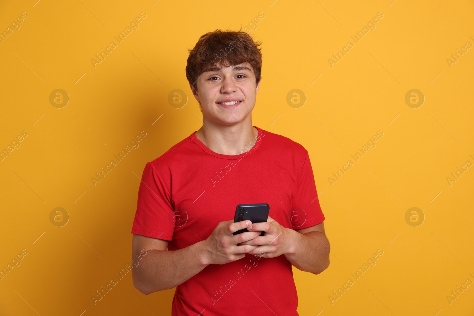 Photo of Portrait of smiling teenage boy with smartphone on yellow background