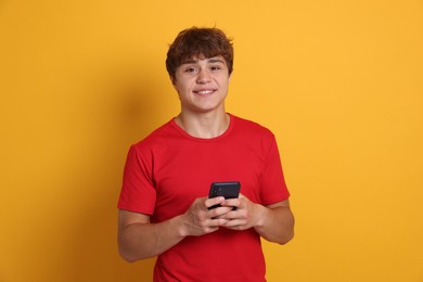 Photo of Portrait of smiling teenage boy with smartphone on yellow background