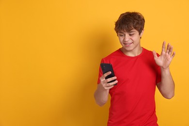 Photo of Smiling teenage boy having videocall by smartphone on yellow background. Space for text