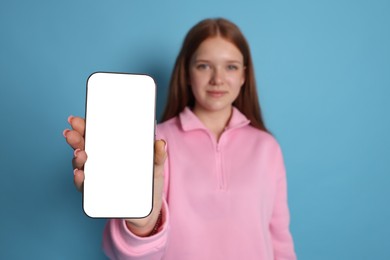 Photo of Beautiful teenage girl showing smartphone with blank screen on light blue background, selective focus. Mockup for design