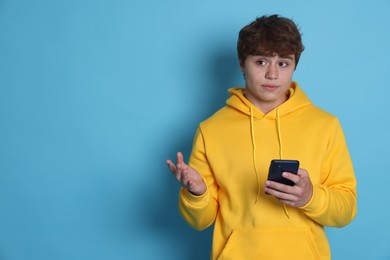 Photo of Teenage boy with smartphone on light blue background. Space for text