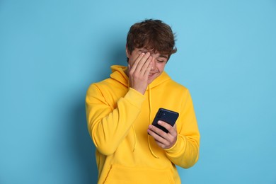 Photo of Smiling teenage boy with smartphone on light blue background