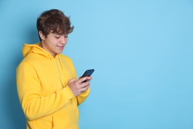 Photo of Smiling teenage boy using smartphone on light blue background. Space for text