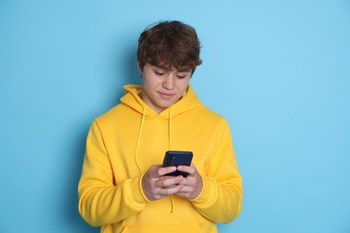 Photo of Teenage boy using smartphone on light blue background