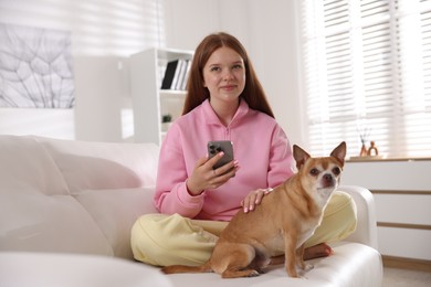 Photo of Beautiful teenage girl with smartphone and dog on sofa at home